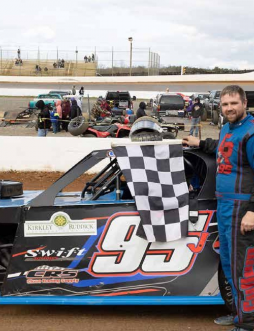 Justin Cullum stands next to his race car on the track.